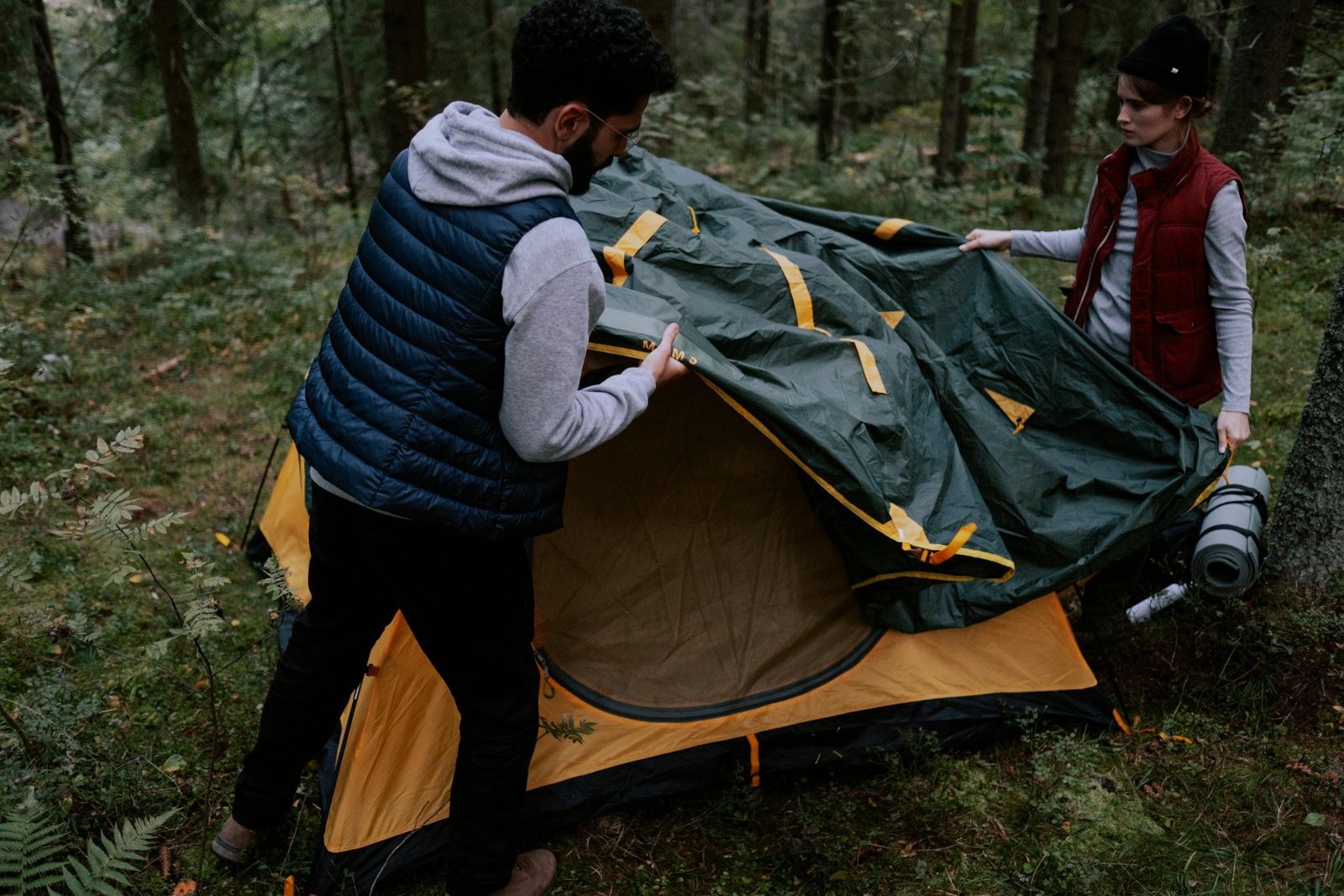 Hero_Section_Image A couple setting up a tent in a forest, enjoying a camping trip.