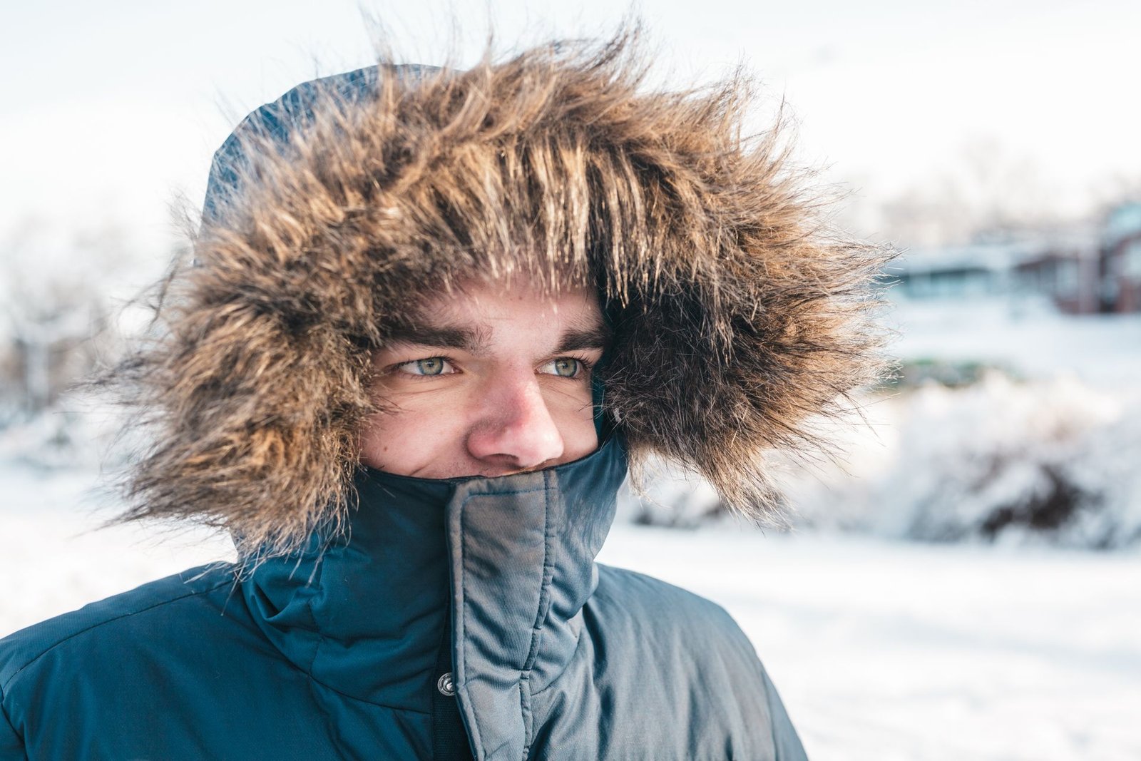 A man wears a fur-lined parka outdoors during winter in a snowy landscape.